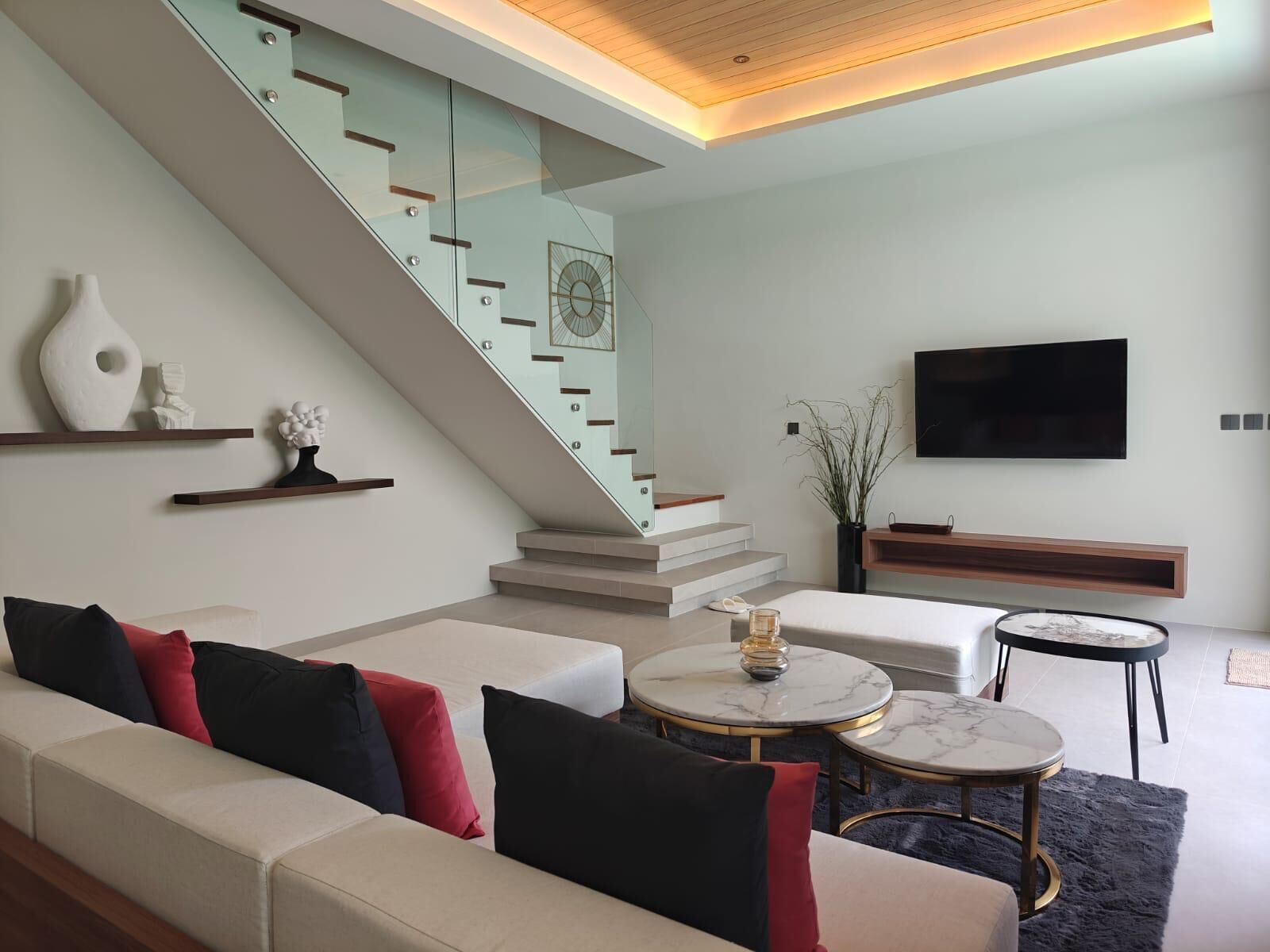 Una sala de estar moderna con una escalera, un conjunto de sofás, un televisor de pantalla plana y una mesa de centro.