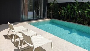 Ein moderner Poolbereich im Freien mit zwei Korbsesseln und einer Glastür, die auf eine überdachte Terrasse führt.