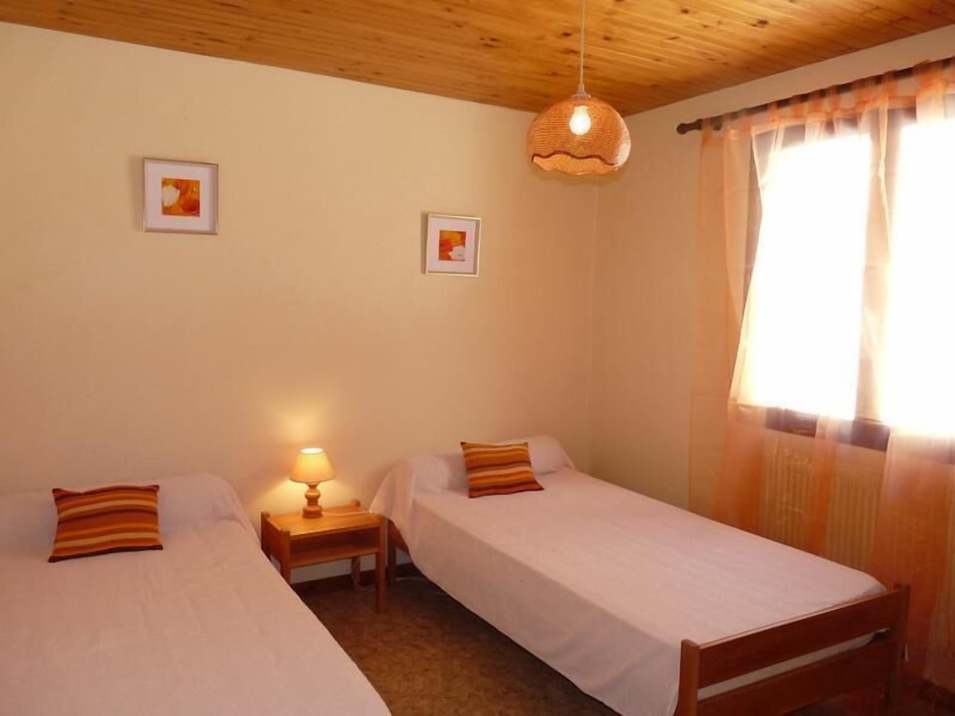 Une chambre avec deux lits simples, un plafond en bois et une fenêtre avec des rideaux.