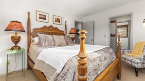 Un dormitorio ordenado con una cama con dosel de madera, dos lámparas de noche, una mesita de noche verde y un sillón a cuadros.