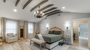 Un dormitorio espacioso con una cama grande, una araña, techo de madera y vista al baño.