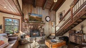 Una sala de estar acogedora con chimenea de piedra, sofás de cuero y una escalera de madera.