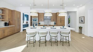 A modern kitchen with wooden cabinets, a central island with bar stools, and pendant lighting. - Vanderbilt Luxury | Private Salt Pool & Spa | Minutes to Vanderbilt Beach (Naples)