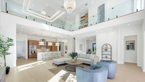 A spacious, modern living area with a high ceiling, a kitchen in the background, and a balcony with glass railings. - Vanderbilt Luxury | Private Salt Pool & Spa | Minutes to Vanderbilt Beach (Naples)