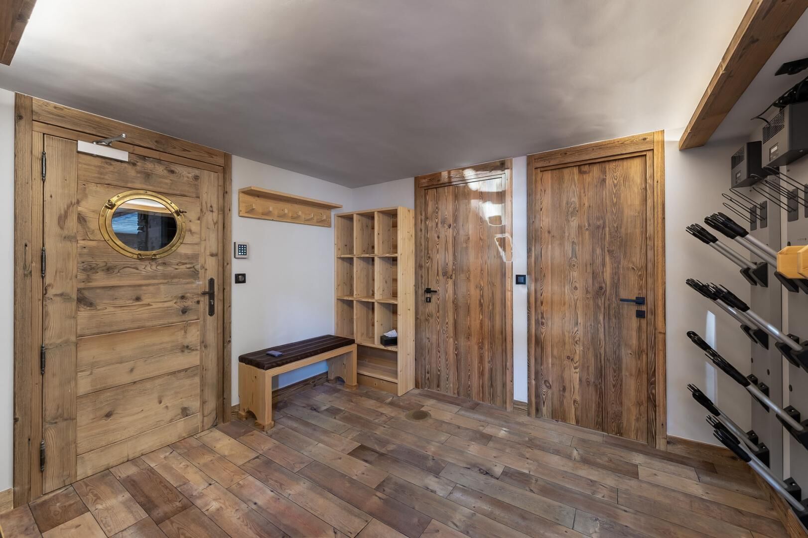 Un pasillo con piso de madera, un banco, puertas de madera y una estantería para vinos.