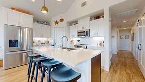Een moderne keuken met witte kasten, roestvrijstalen apparatuur, een centraal eiland met barkrukken en decoratieve elementen zoals een zeester en een bord.'