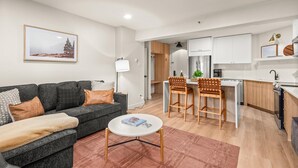 A modern living room with a gray sofa, a round coffee table, and a kitchen area with white cabinets and a wooden dining table. - 🏔️Brand New Listing~Studio Premier 204🏔️ (Snowmass Village)