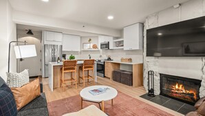 A modern living room with a fireplace, a kitchen with white cabinets, and a dining area with two wooden chairs. - 🏔️Brand New Listing~Studio Premier 204🏔️ (Snowmass Village)