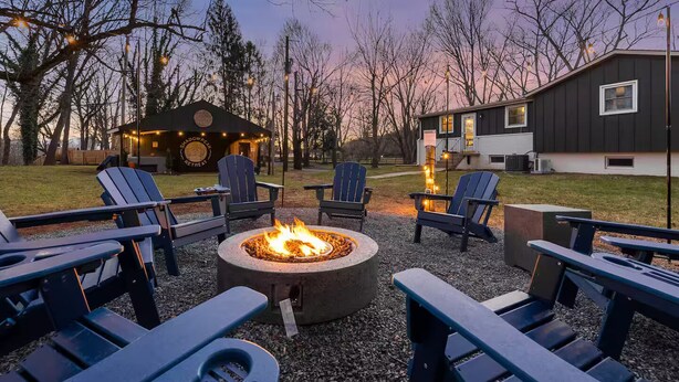 An outdoor seating area with Adirondack chairs and a fire pit, surrounded by trees and a building with a sign that reads "Shadow Peak Retreat." - Riverfront- 3 Hole Golf Course - Pool - Hot Tub - Sauna - 2 Game Rooms (Elkton)