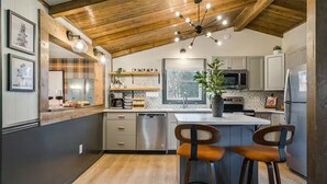 A modern kitchen with wooden ceiling beams, a central island with bar stools, stainless steel appliances, and a window providing natural light. - Riverfront- 3 Hole Golf Course - Pool - Hot Tub - Sauna - 2 Game Rooms (Elkton)