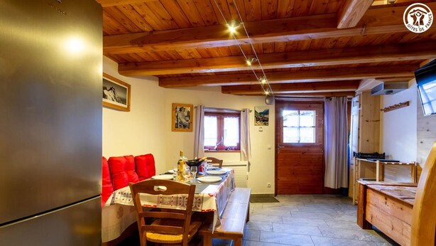 A cozy kitchen with wooden beams, a dining table with red cushions, and a refrigerator. - LA MAISON DU PAPE - BONNEVAL SUR ARC (BONNEVAL SUR ARC)