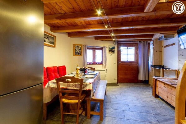 Una cocina acogedora con vigas de madera, una mesa de comedor con cojines rojos y un refrigerador.
