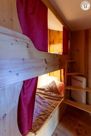 Un lit superposé avec un rideau rouge, des murs en bois et une échelle.