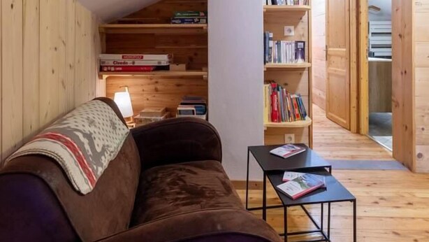 Una sala de estar acogedora con un sofá morado, estanterías de madera y una pequeña mesa.
