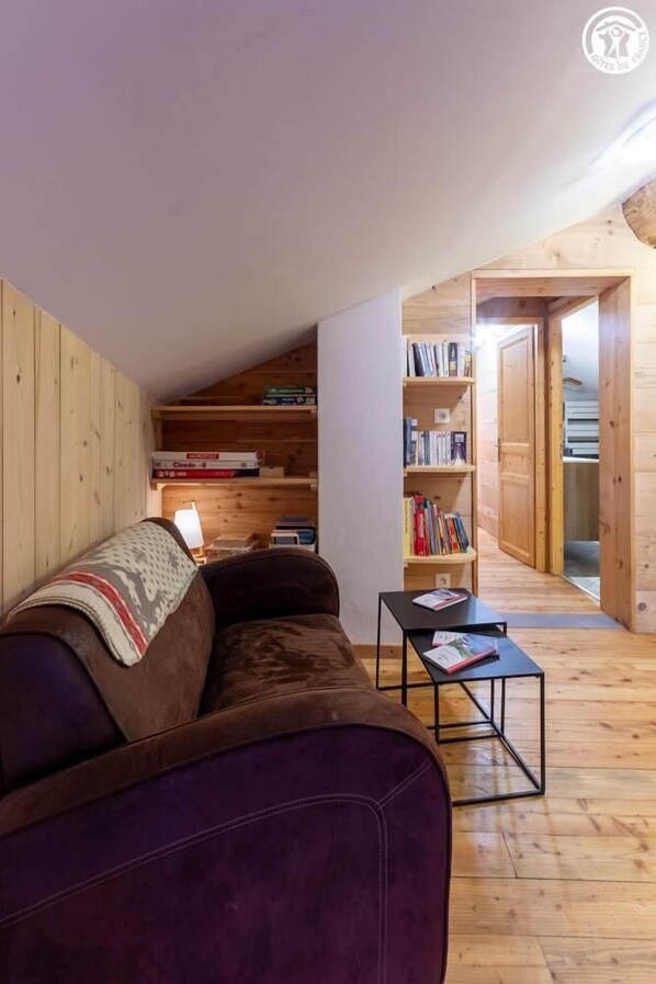 Een gezellige woonkamer met een paarse bank, houten boekenkasten en een kleine tafel.
