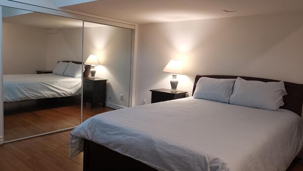 A bedroom with a bed, two bedside tables with lamps, a large mirror, and a wooden floor.