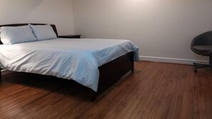 A bedroom with a bed, a chair, and wooden flooring.