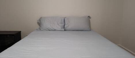 A single bed with white bedding in a room with plain walls.