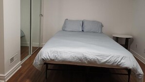 A bedroom with a bed, a small table, and a sliding glass door leading to another room.