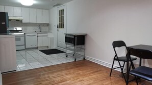 A kitchen with white cabinets, a refrigerator, a microwave, and a sink. There is a dining table with two chairs and a small cart.
