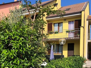 Ein gelbes Gebäude mit Balkon, umgeben von viel Grün.