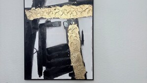 A modern art piece with black and gold abstract designs on a white wall.