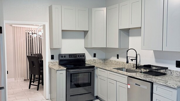 A modern kitchen with white cabinets, a granite countertop, a stainless steel stove, and a dishwasher.