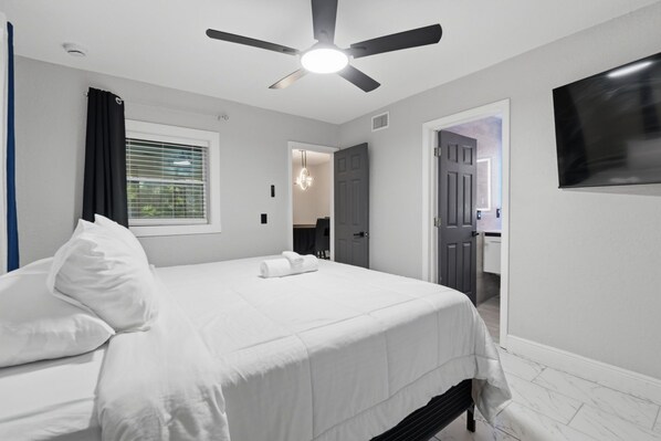 A bedroom with a bed, a ceiling fan, a window with blinds, and a door leading to a bathroom.