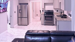 A modern kitchen with white cabinets, stainless steel appliances, and a black leather sofa in the foreground.