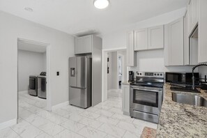 A modern kitchen with stainless steel appliances, white cabinetry, and a marble floor.