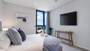 Ett modernt sovrum med en stor säng, en platt-TV och ett fönster med utsikt över byggnader.