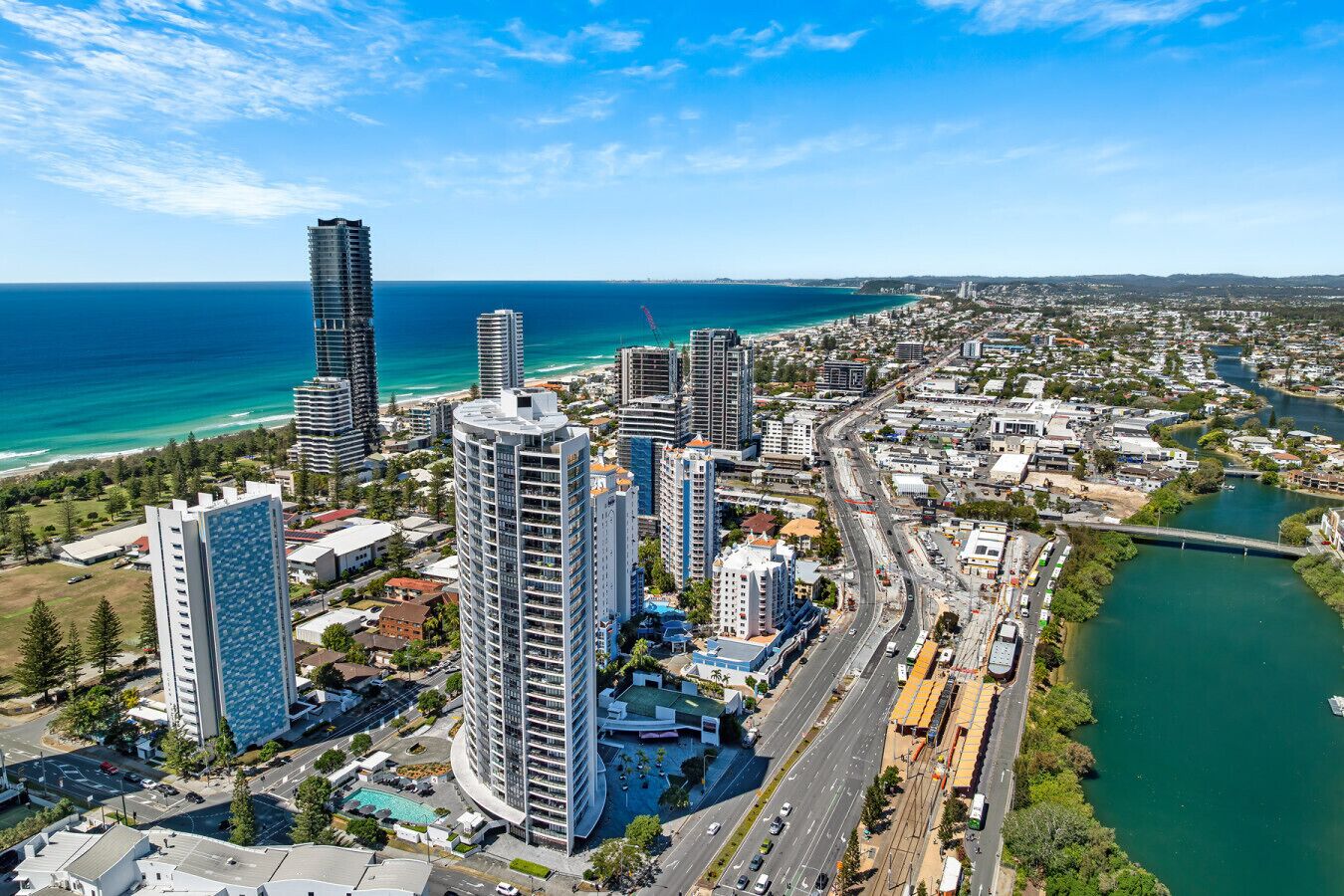 A high-rise hotel with multiple floors, a swimming pool, and a view of the coastline.