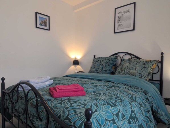 A neatly made bed with a floral bedspread, a black metal headboard, and two framed pictures on the wall.