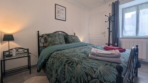 A bedroom with a bed, a nightstand, a lamp, a window with curtains, and a door. - Au petit Café - Châteauvillain (Châteauvillain)