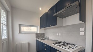 A modern kitchen with dark blue cabinets, a gas stove, and a window with a view of the outside. - Au petit Café - Châteauvillain (Châteauvillain)