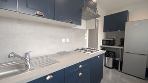 A modern kitchen with a gas stove, stainless steel sink, and dark blue cabinets. - Au petit Café - Châteauvillain (Châteauvillain)