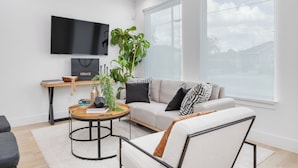 Ein modernes Wohnzimmer mit einer Couch, einem Couchtisch, einem an der Wand befestigten Fernseher und einem großen Fenster.