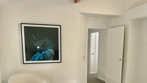A room with a white armchair, a framed picture on the wall, and a door leading to another room.