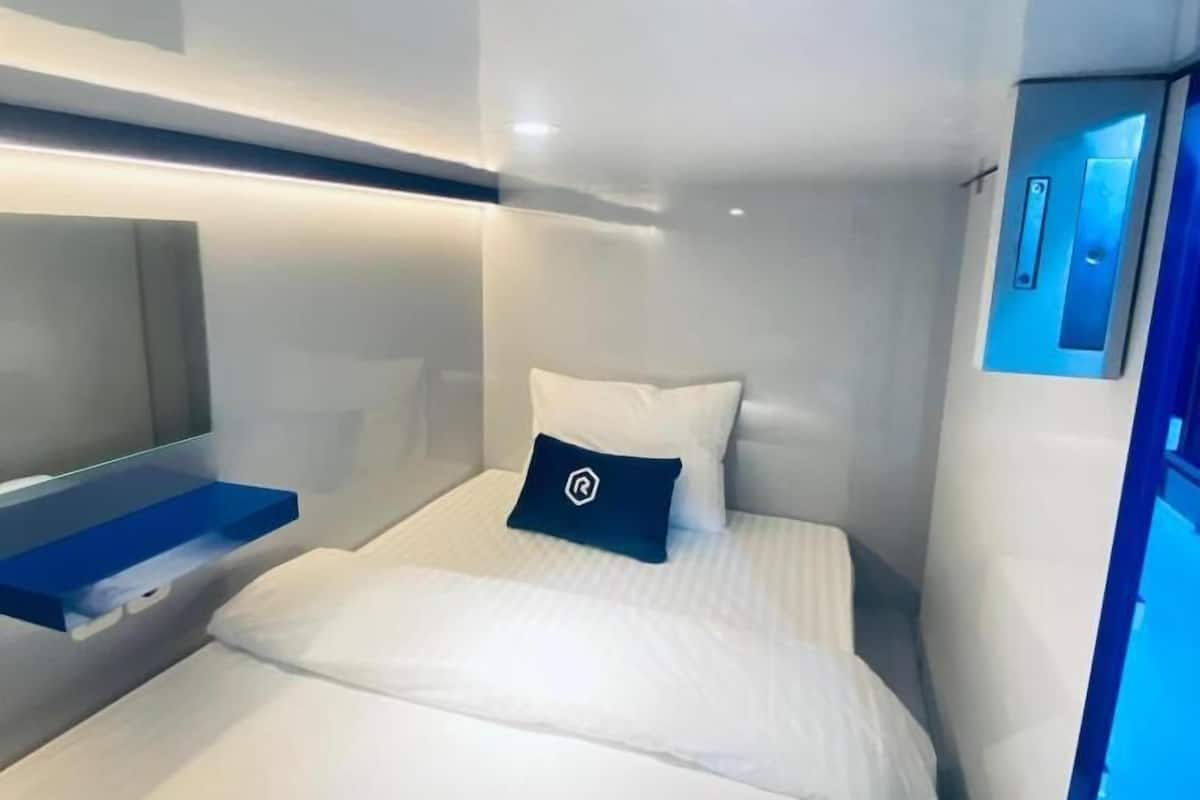 A modern hotel room with a bed, a bedside table, a built-in shelf, and a wall-mounted control panel.