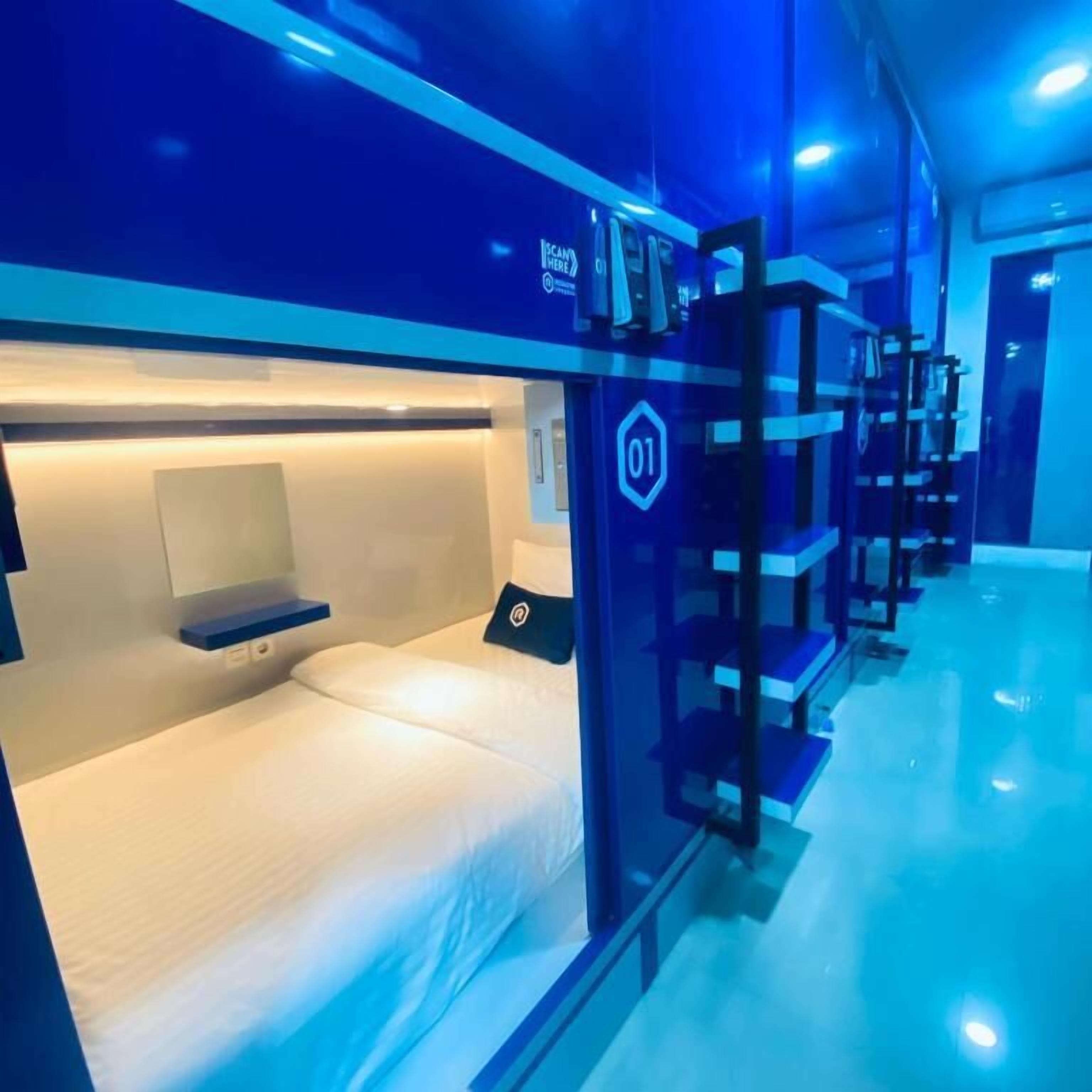 Una habitación de hotel moderna con una cama litera, un escritorio pequeño y una pantalla digital que muestra '01'.