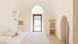 Ein schlicht eingerichtetes Schlafzimmer mit einem großen Bett, einer Tür, die nach draußen führt, und einem kleinen Regal.
