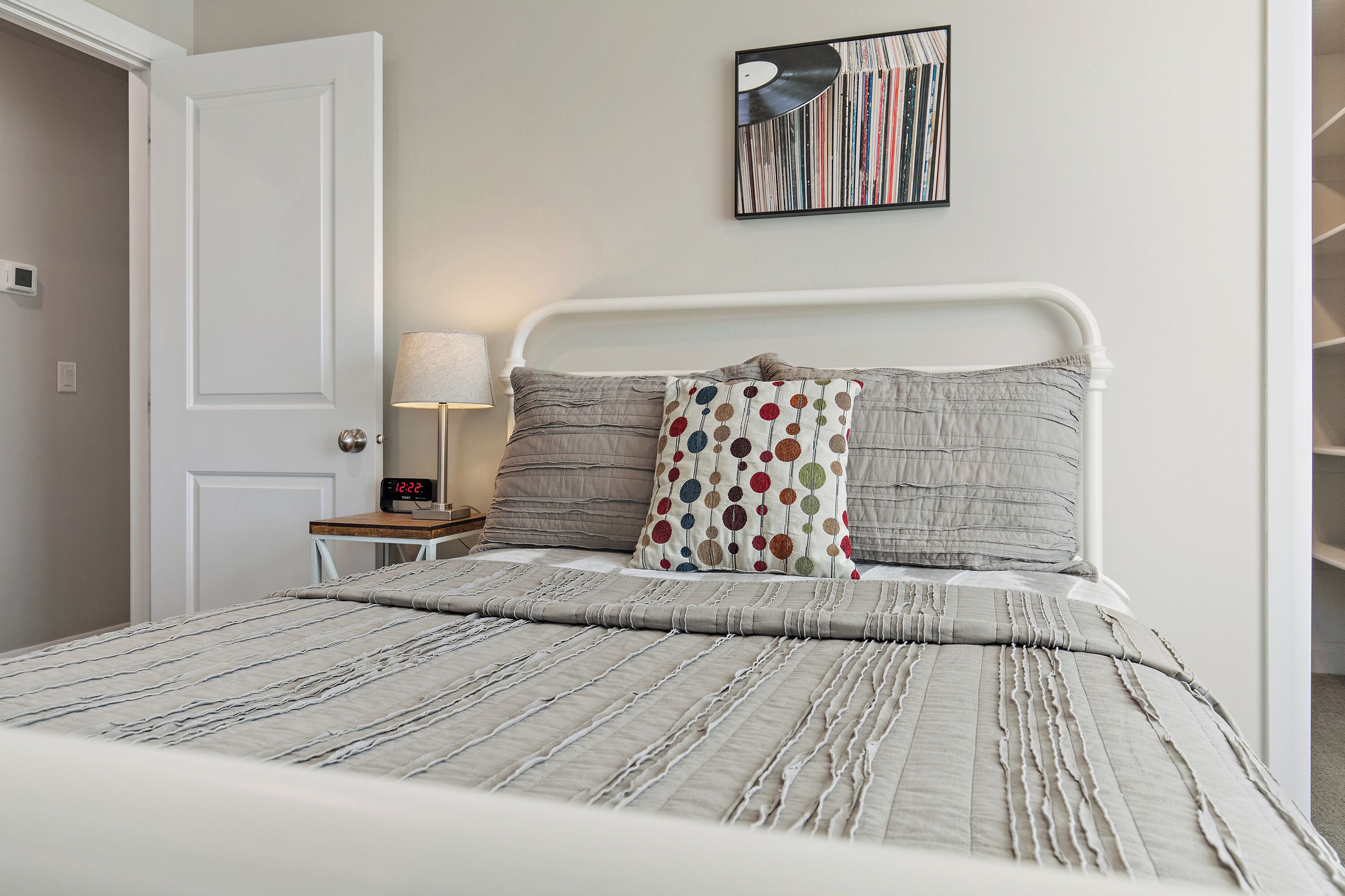 A neatly made bed with a striped bedspread and pillows, a bedside table with a lamp, and a wall-mounted artwork.