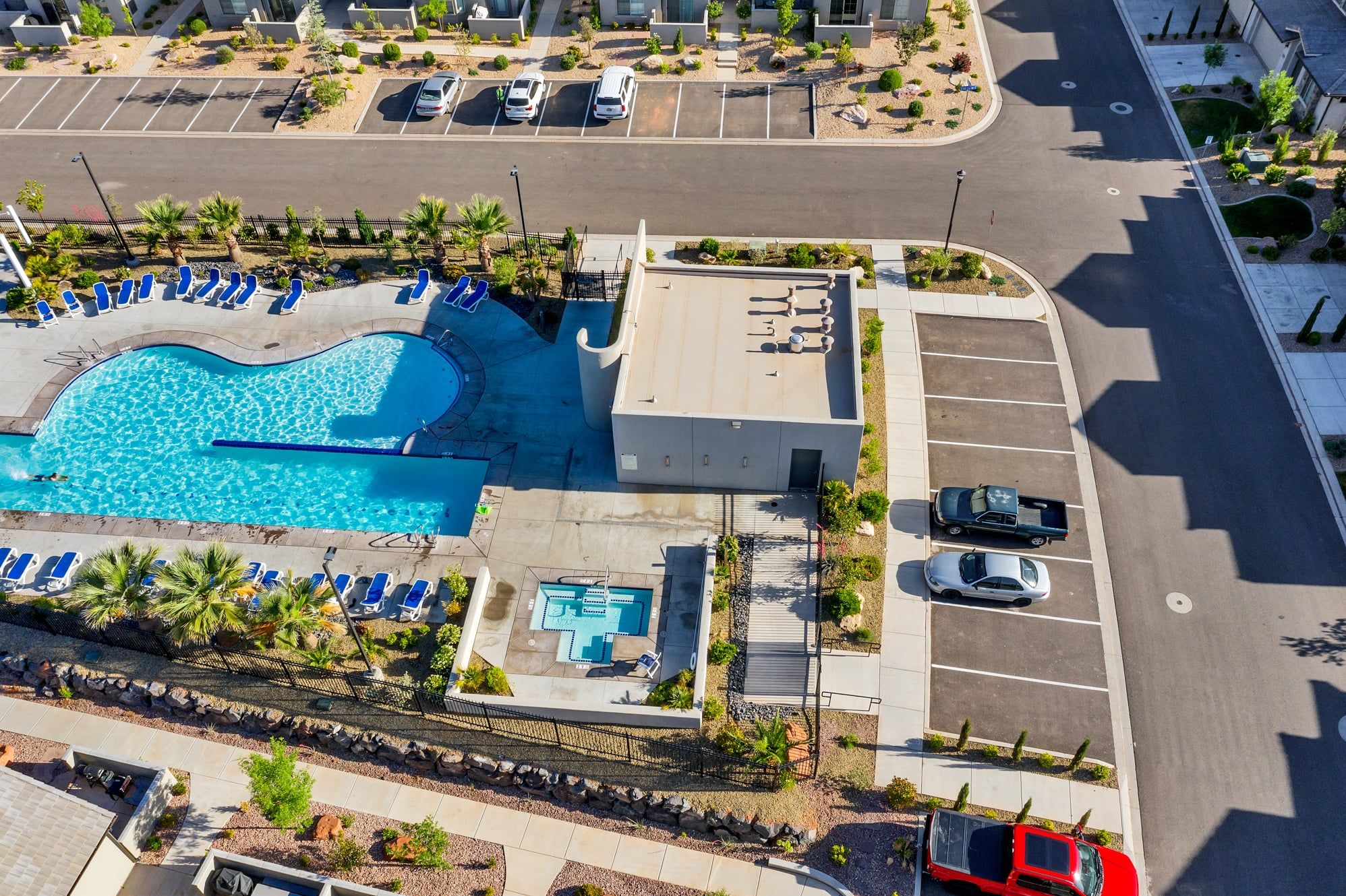 An aerial view of a hotel with a swimming pool, parking area, and a landscaped garden.