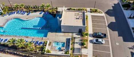 An aerial view of a hotel with a swimming pool, parking area, and a landscaped garden.