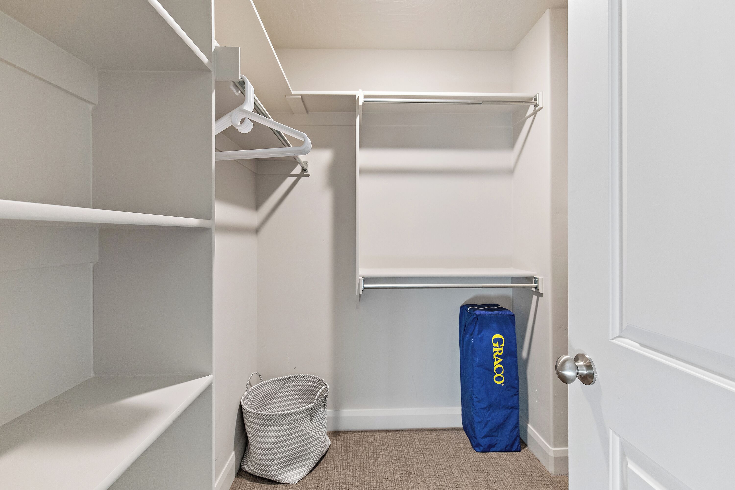 Um closet amplo com prateleiras brancas, uma barra para pendurar roupas e uma bolsa azul com a etiqueta "GRACO".