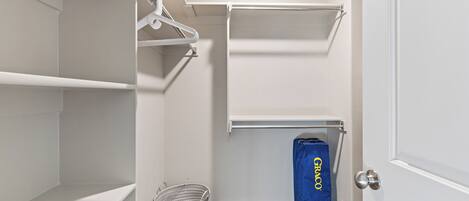 Um closet amplo com prateleiras brancas, uma barra para pendurar roupas e uma bolsa azul com a etiqueta "GRACO".