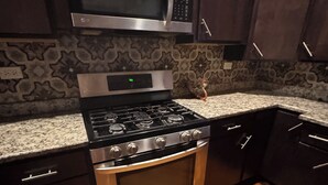 A kitchen with a stainless steel stove, oven, and microwave, dark wooden cabinets, and a patterned backsplash. - Peaceful 1-bedroom apartment with AC in vibrant Chicago (Chicago)