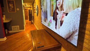 A hallway with wooden flooring, a mounted television displaying a scene, and a small table with a keychain. - Peaceful 1-bedroom apartment with AC in vibrant Chicago (Chicago)