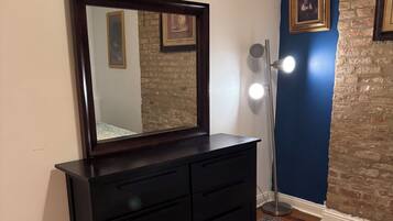 Quarto com penteadeira de madeira escura, um espelho grande, tapete estampado e uma parede azul de destaque.