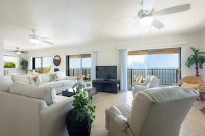 A spacious living room with a balcony, a ceiling fan, and a television. - Gulfside Gem   2bed/2bath Open Water Waterfront Escape (Marathon)